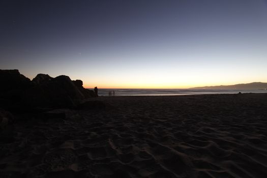 A tranquil beach scene at twilight with silhouettes on the horizon and a calm ocean.