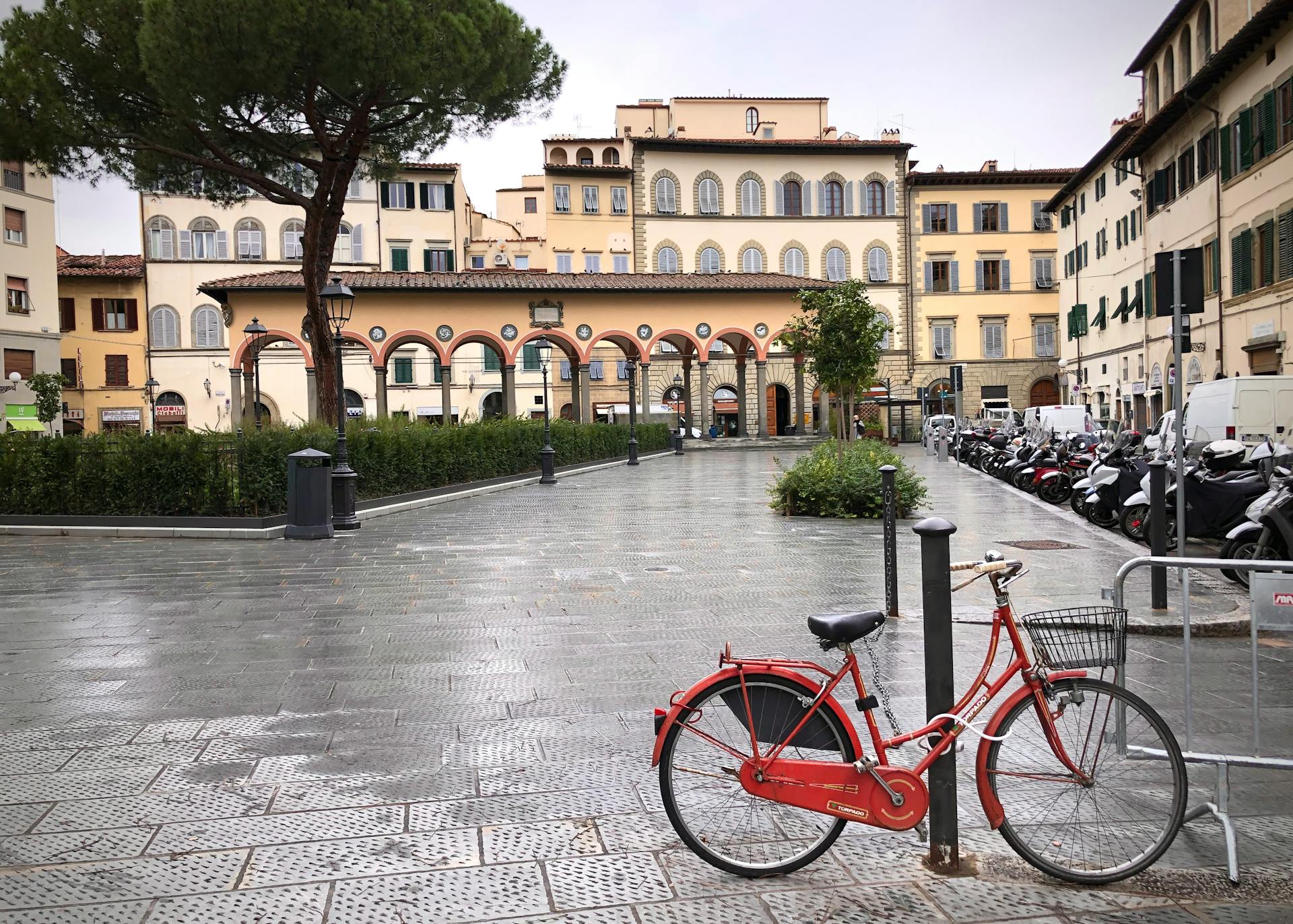 A tranquil view of Piazza dei Ciompi in Florence featuring a locked red bike against historic architecture.