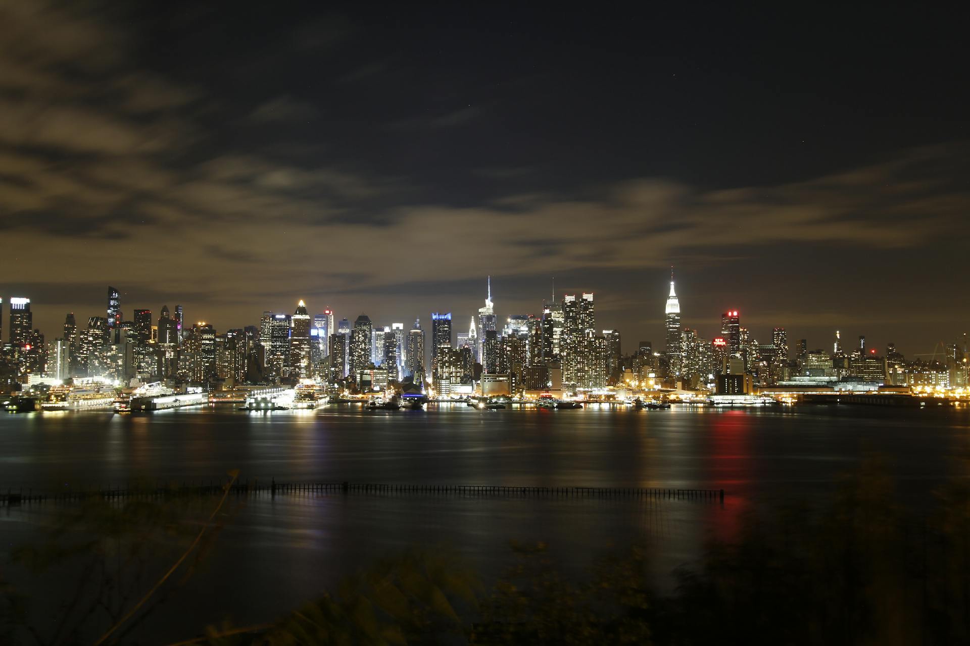 A breathtaking panoramic view of New York City skyline at night, showcasing illuminated buildings and reflections in the river.