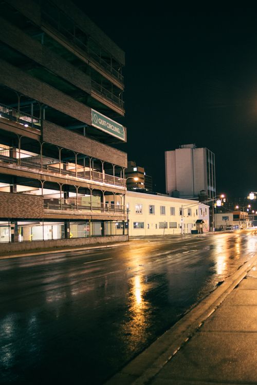 Free Town district with modern illuminated buildings and asphalt road near pavement at night under dark cloudless sky Stock Photo