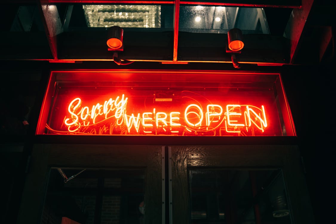 Illuminated red signboard with inscription Sorry We Are Open of modern building of nightclub