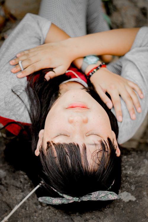 Free A serene image of a woman lying on the ground outdoors with eyes closed and arms crossed. Stock Photo