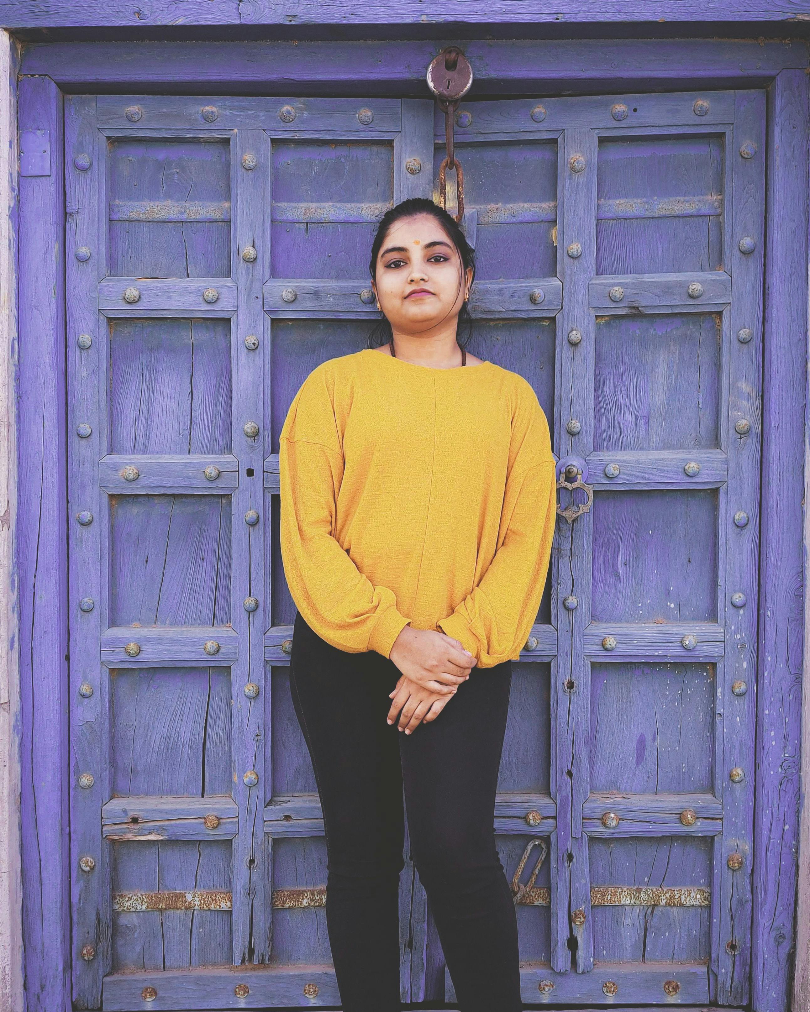 Confident woman in yellow sweater standing against a rustic blue wooden door.