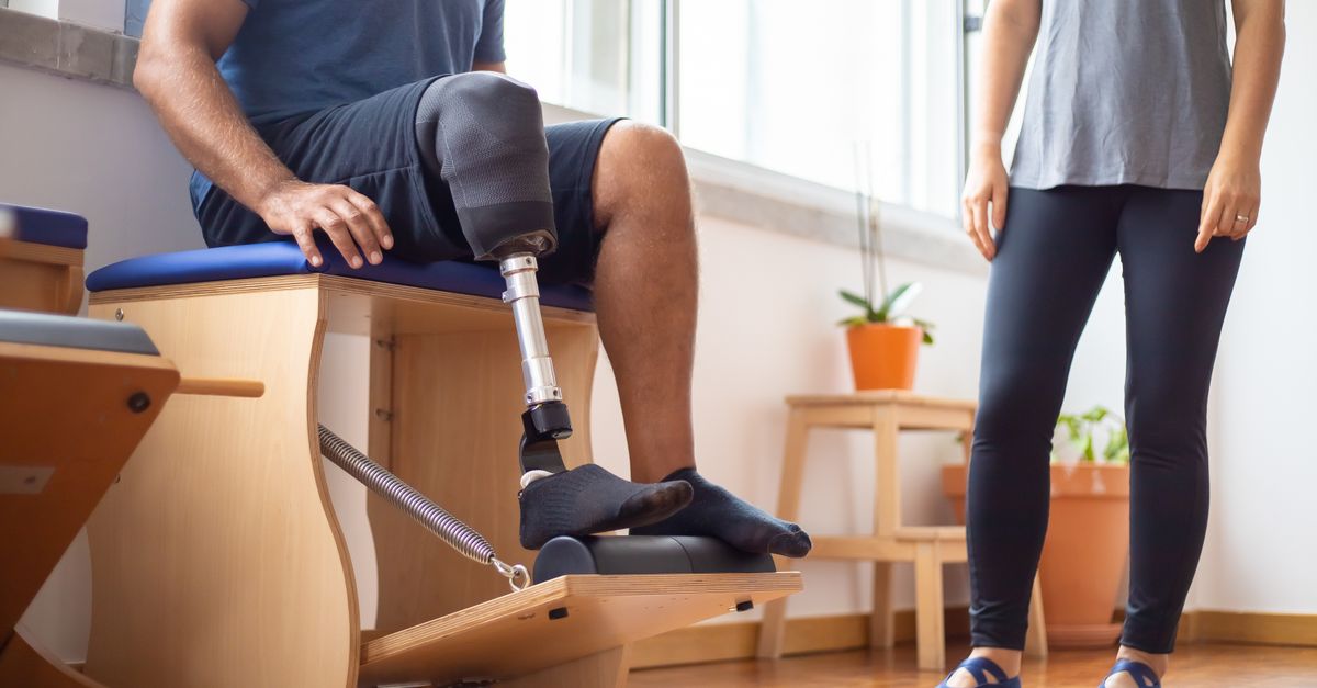 Man using prosthetic leg during rehabilitation exercise with trainer in gym setting.