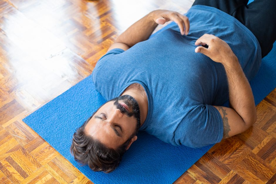 Como Superar a Ansiedade com Técnicas de Respiração Simples 2 Adult man lying on a blue yoga mat indoors with eyes closed, focusing on relaxation and mindfulness.