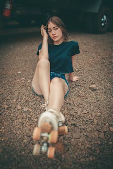 Stylish young woman sitting on gravel, posing with roller skates. Perfect for lifestyle imagery.