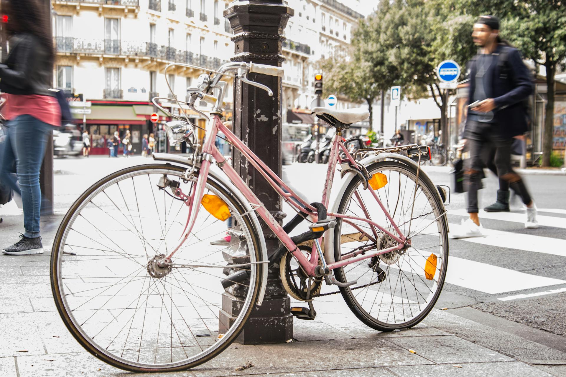 Pink bicycle locked to a post on a bustling Paris street with pedestrians in motion.