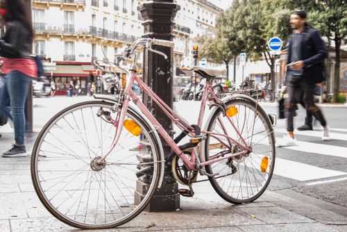 Free Pink bicycle locked to a post on a bustling Paris street with pedestrians in motion. Stock Photo