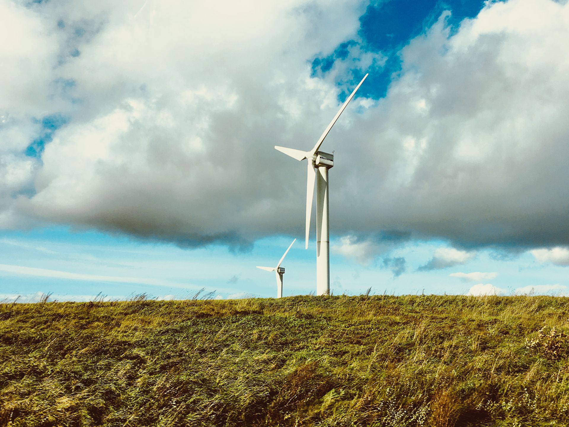 Wind turbines generating renewable energy in a rural Lithuanian landscape under a cloudy sky.