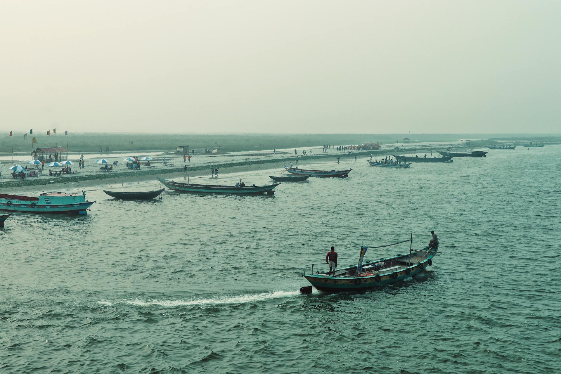 Aerial shot of boats navigating the Meghna River in Chandpur, Bangladesh, with people onshore.