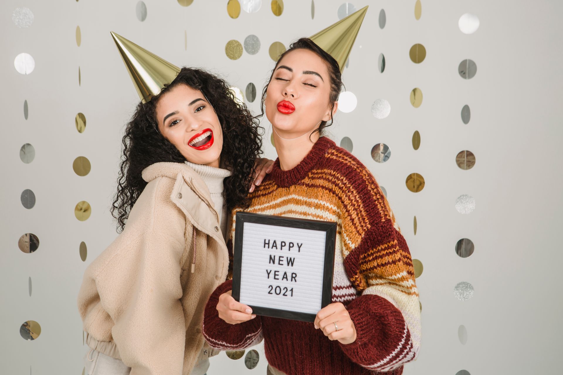 Two women wearing party hats celebrating New Year 2021 with a festive sign.