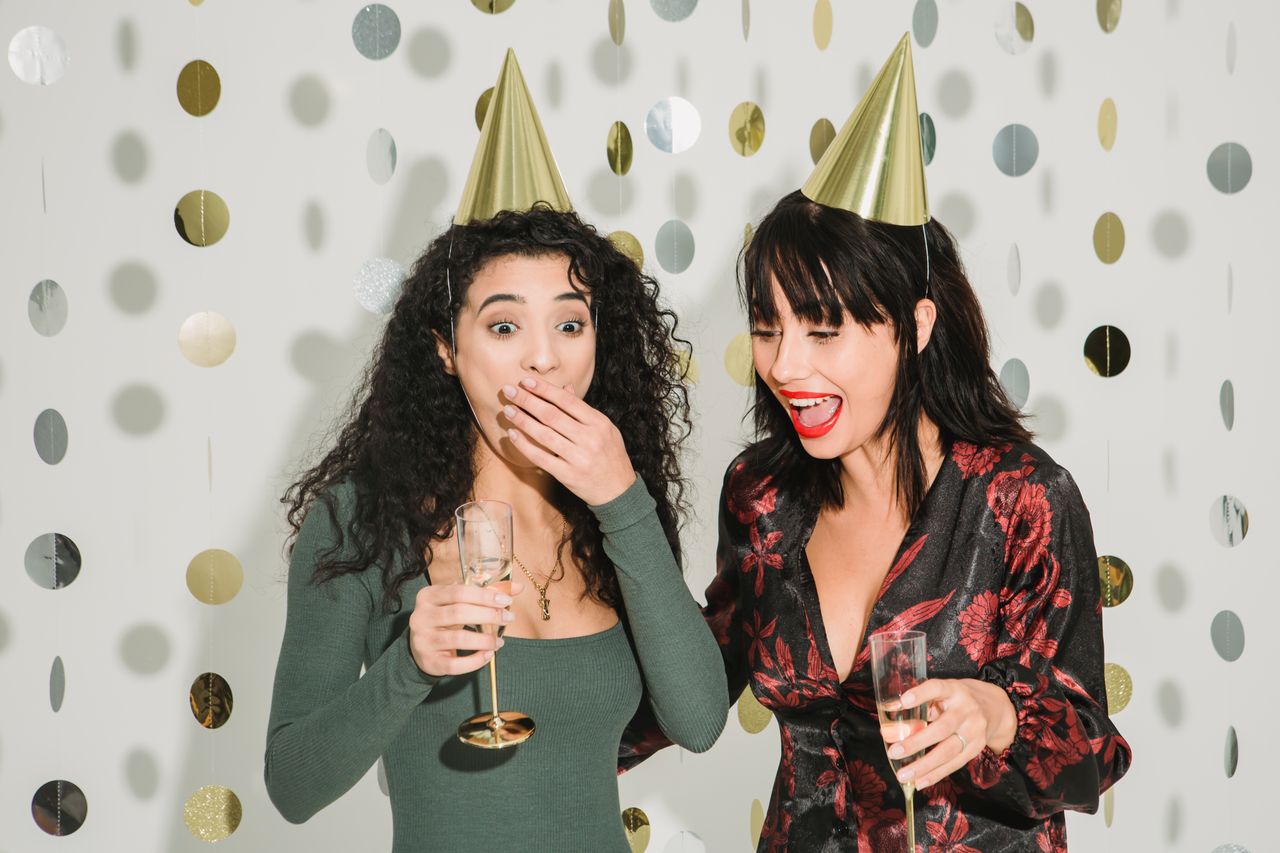 surprised woman covering mouth while standing with glass of champagne