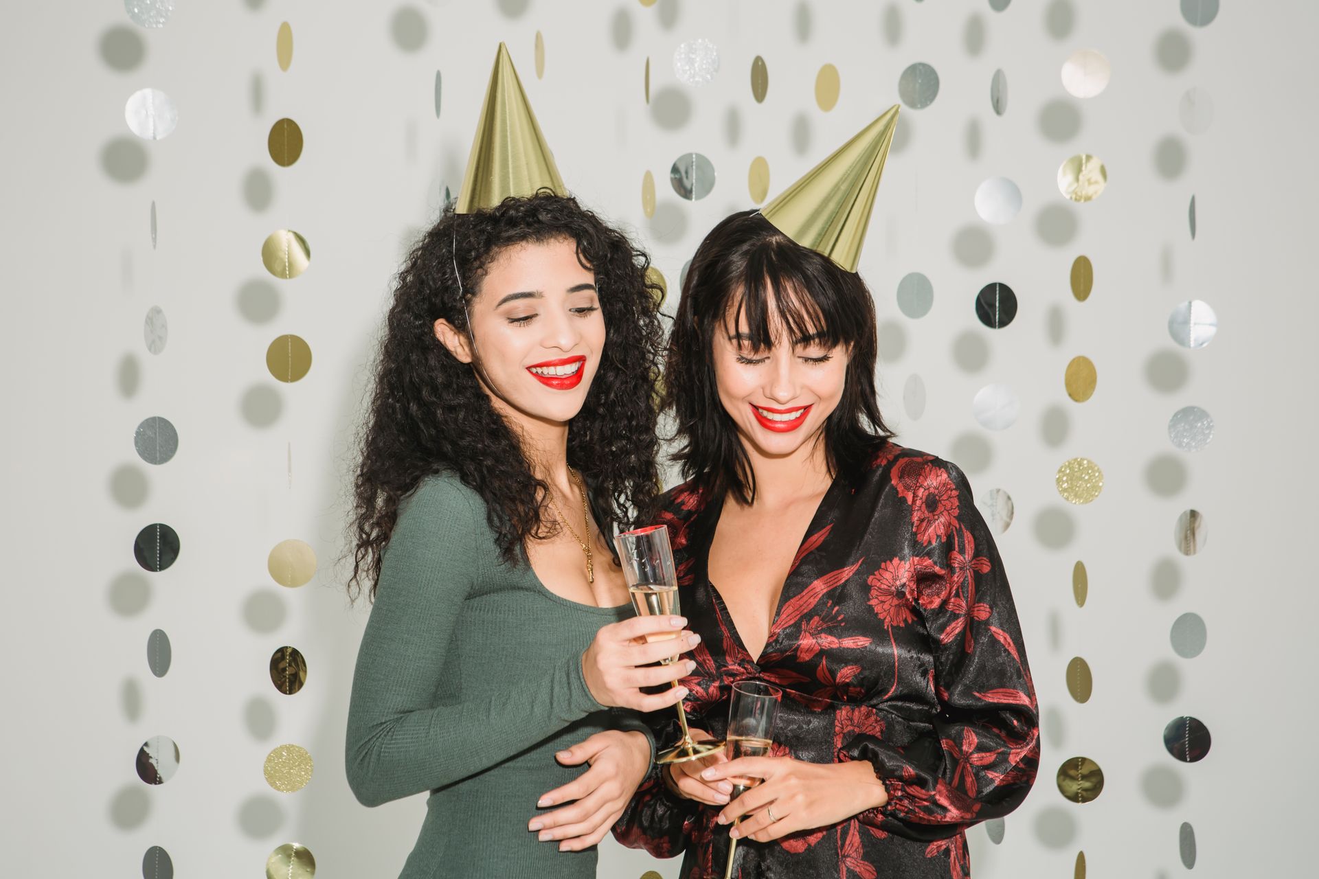 Two women celebrating indoors with party hats and drinks, full of smiles and joy.