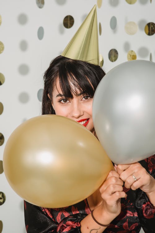 Happy woman in birthday cap with silver and golden balloons