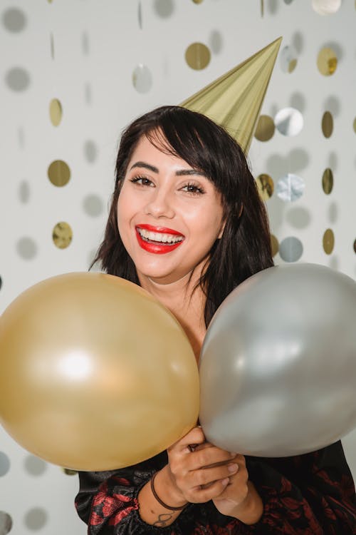 Cheerful woman in birthday cap with silver and golden balloons