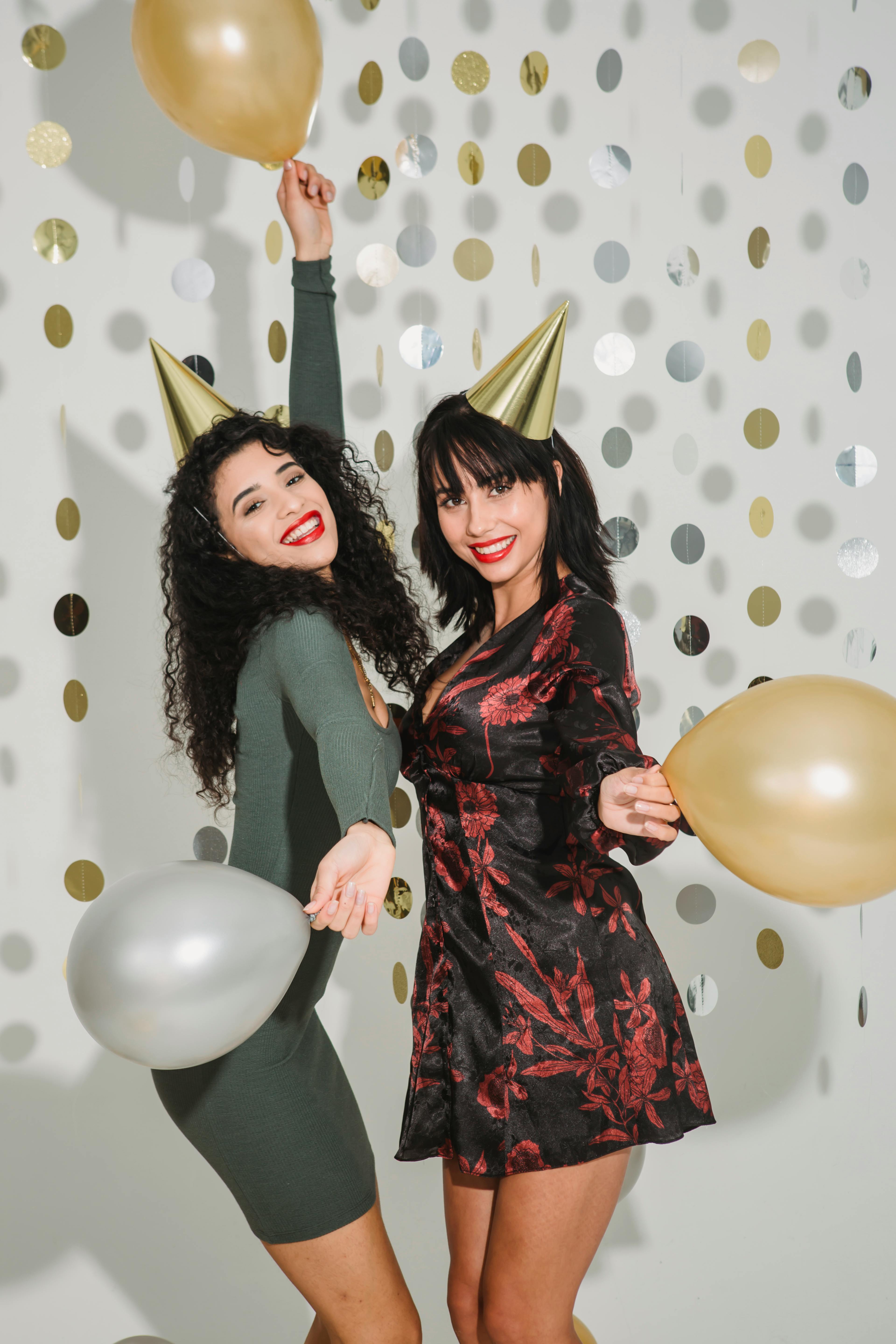 slim women in dresses and golden birthday caps with balloons