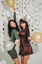Young friends with red lips in golden birthday caps dancing with balloons among confetti
