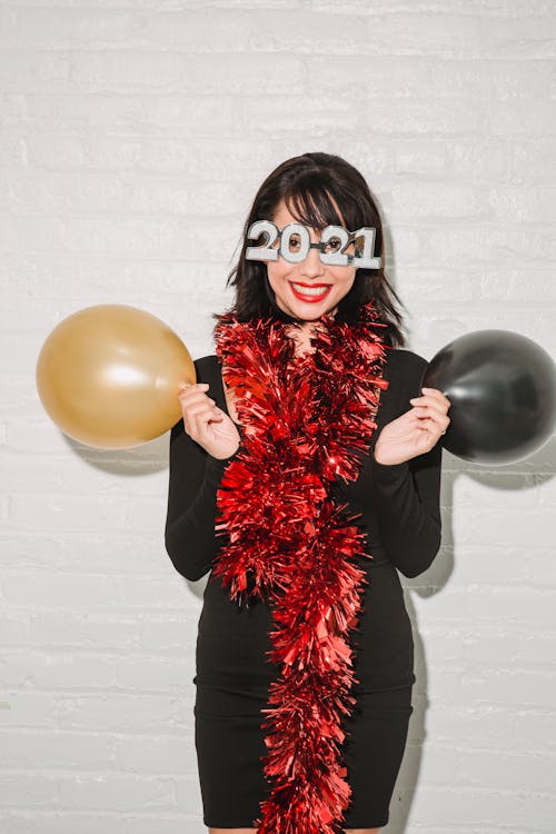 Positive woman in festive glasses and tinsel with balloons