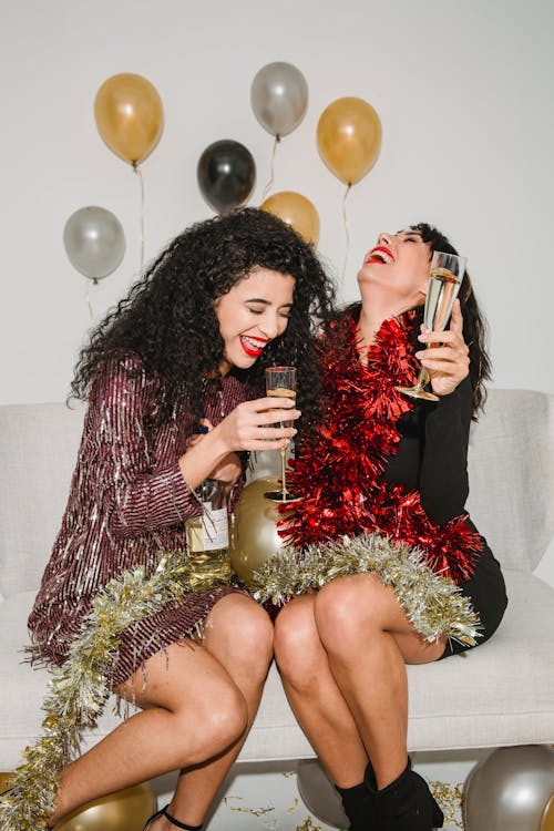 Happy women with champagne and tinsel laughing near balloons