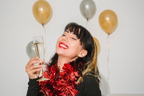 Cheerful young female with closed eyes in tinsel among silver and golden balloons at special event