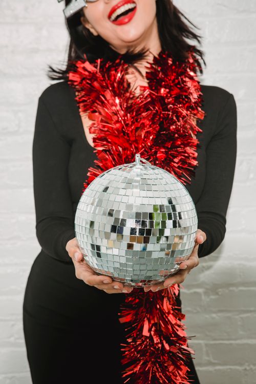Free Crop anonymous cheerful female with red lips in tinsel showing sparkling bright mirror ball and smiling Stock Photo
