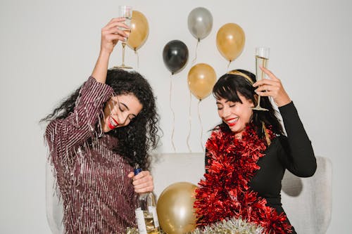 Cheerful friends with glasses of tasty champagne smiling and congratulating each other among balloons