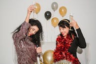 Cheerful friends with glasses of tasty champagne smiling and congratulating each other among balloons