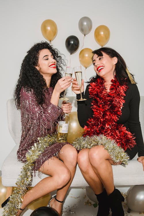 Happy women in sparkling tinsel clinking with glasses of champagne