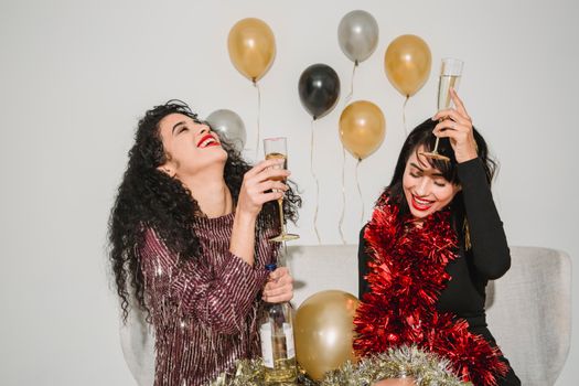 Happy smiling friends with bright red lips and glasses of crystal champagne and red sparkling tinsel celebrating New Year