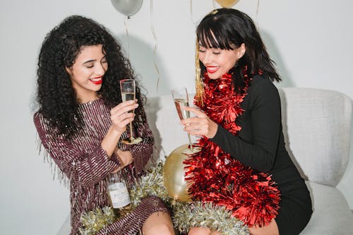 Joyful women with red lips in festive outfits drinking champagne