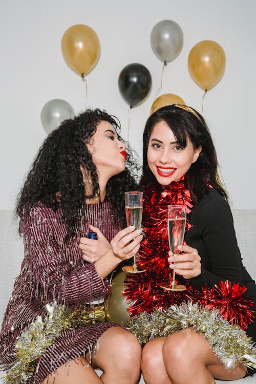 Happy young friends in festive dresses and sparkling bright tinsel entertaining at party among balloons