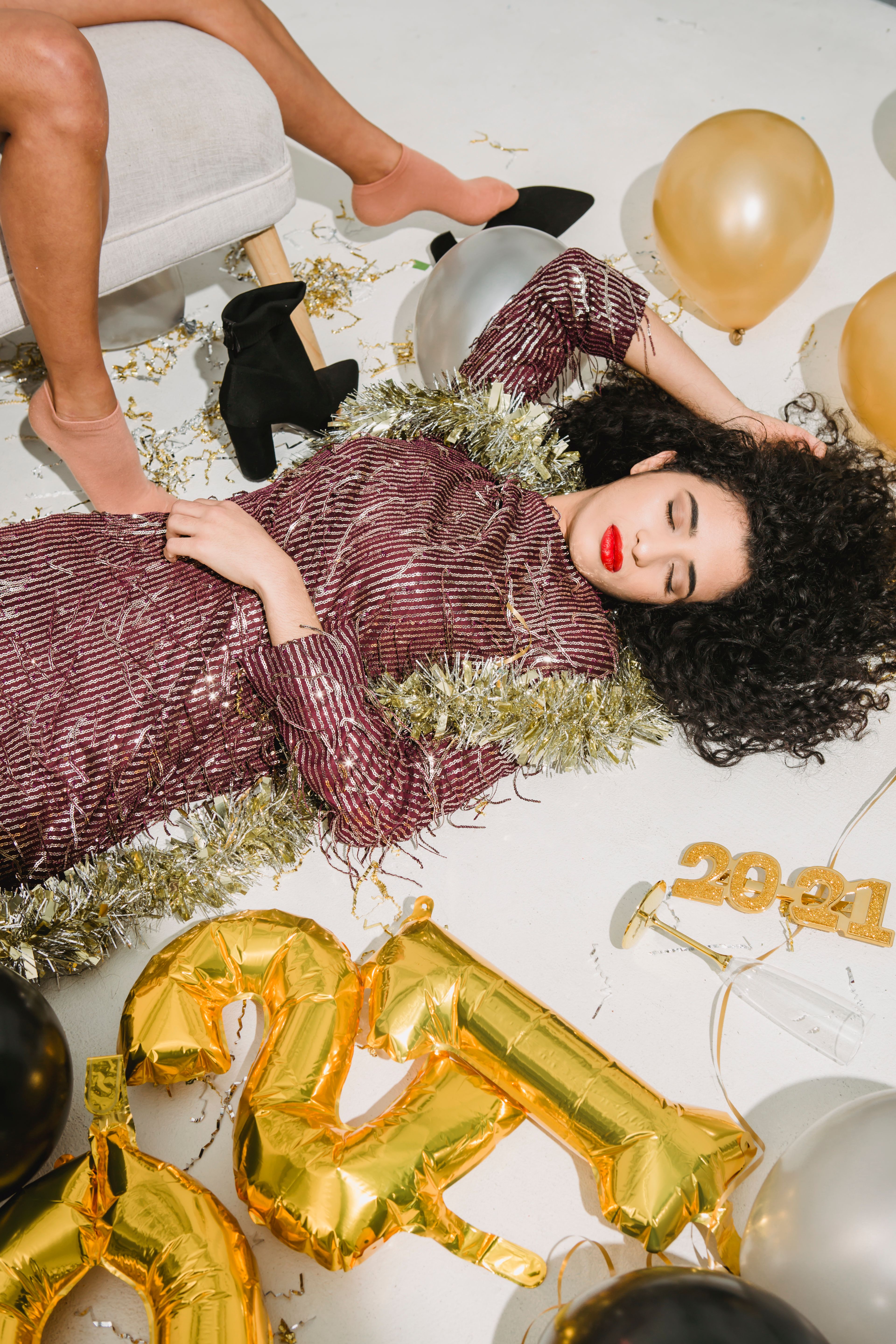 Woman in festive attire surrounded by balloons celebrating New Year's indoors.