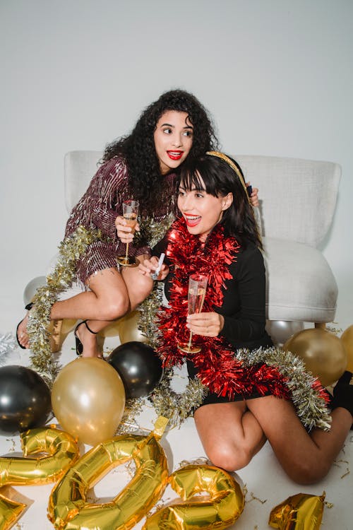 Happy young friends with glasses of champagne enjoying New Year among sparkling tinsel and balloons