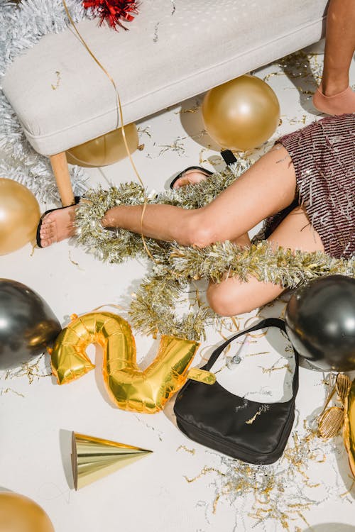 From above of crop anonymous drunk female in festive dress resting among balloons after party