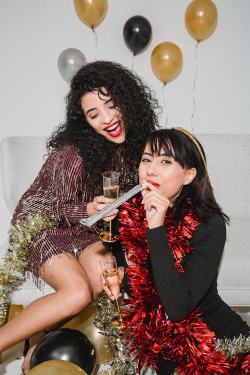 Young happy friends in festive red and golden tinsel drinking champagne while spending time at party