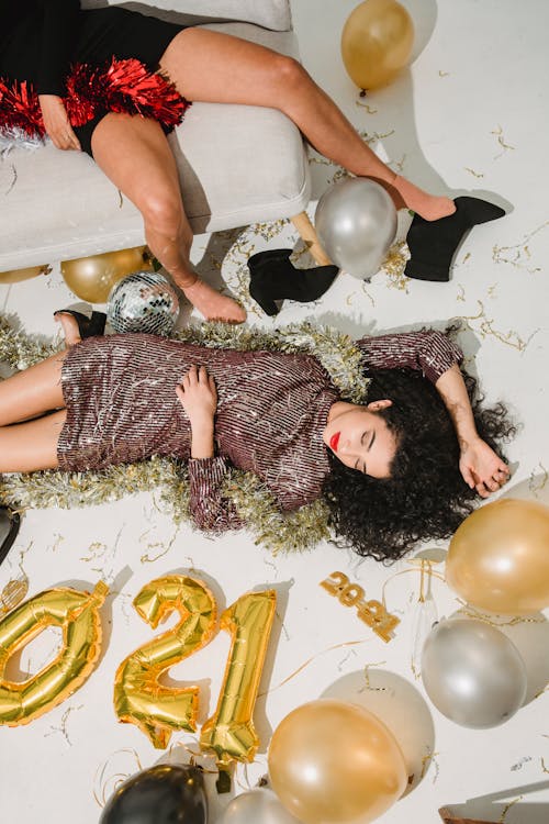 From above of drunk friends relaxing and sleeping among golden and silver balloons after festive celebration of New Year