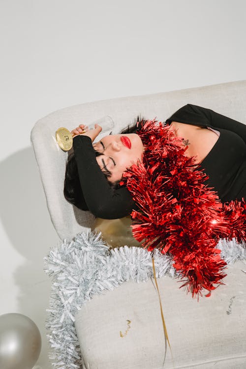 Free Drunk woman with tinsel on neck lying on sofa in light room Stock Photo