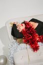 Drunk woman with tinsel on neck lying on sofa in light room