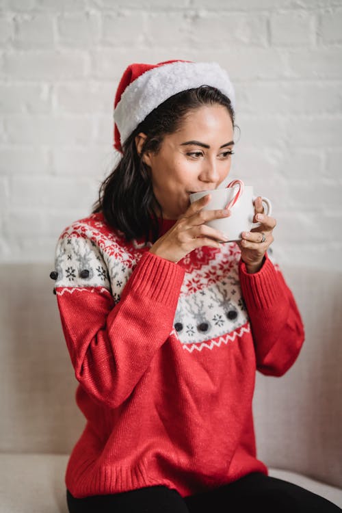 Happy female in festive outfit drinking tasty beverage in apartment