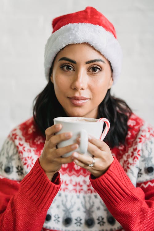 Charming woman in Christmas outfit drinking cup of tasty coffee