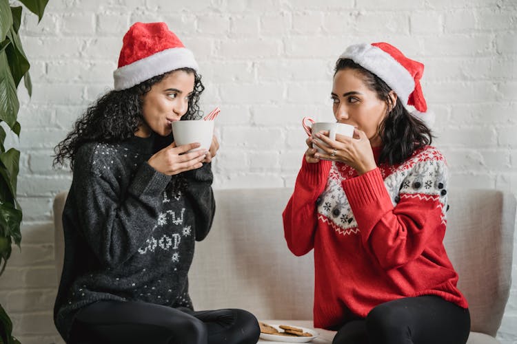 Multiracial Girlfriends Sitting On Sofa At Home And Drinking Cocoa