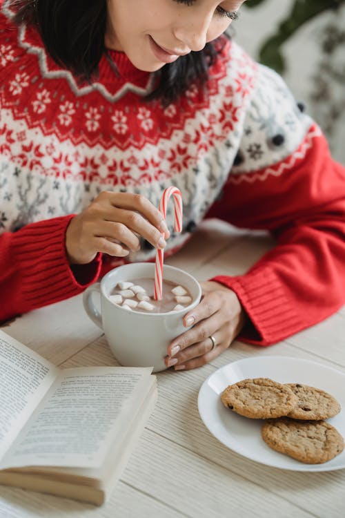 Person in Red Christmas Sweater Holding White Ceramic Cup With Hot Chocolate Drink 