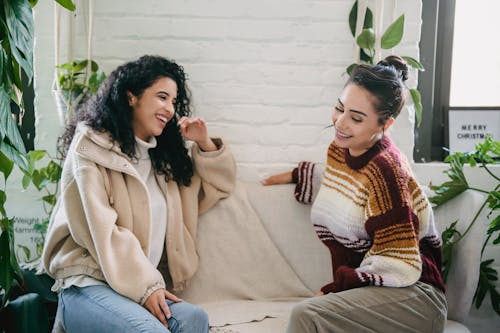 Side view of young woman in casual clothes sitting on sofa and talking while spending weekend together