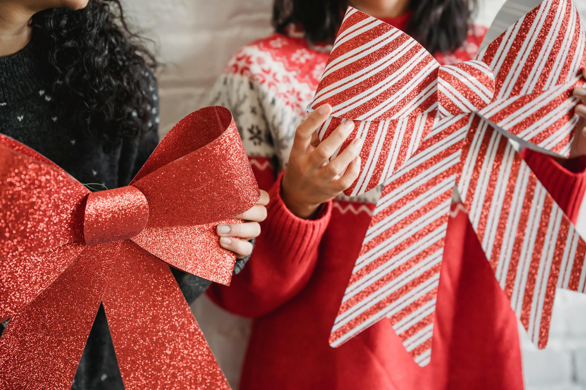 Two women holding large festive red Christmas bows indoors, celebrating the holiday season.