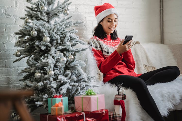 Happy Woman Using Smartphone Near Christmas Tree