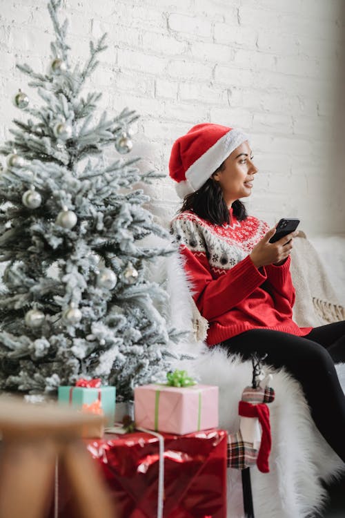 Happy woman browsing smartphone near Christmas tree in house