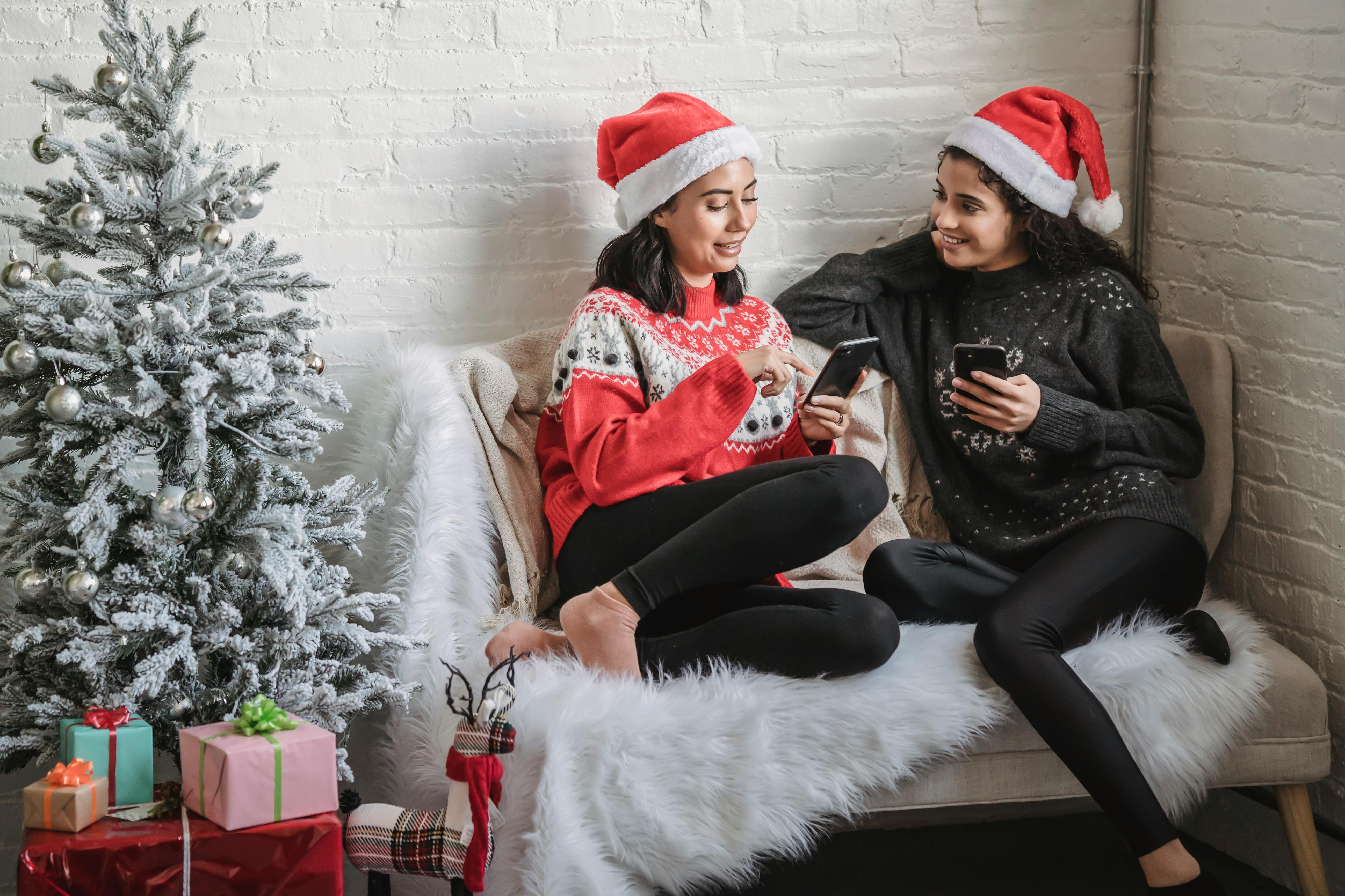 cheerful women using smartphones while celebrating christmas holiday at home