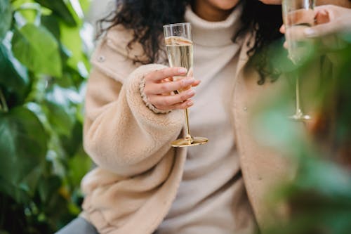 Anonymous female in smart casual clothes with glass of champagne celebrating occasion with friend