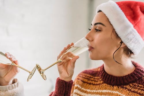 Female in Santa hat drinking champagne from glass while celebrating New Year at home with friend