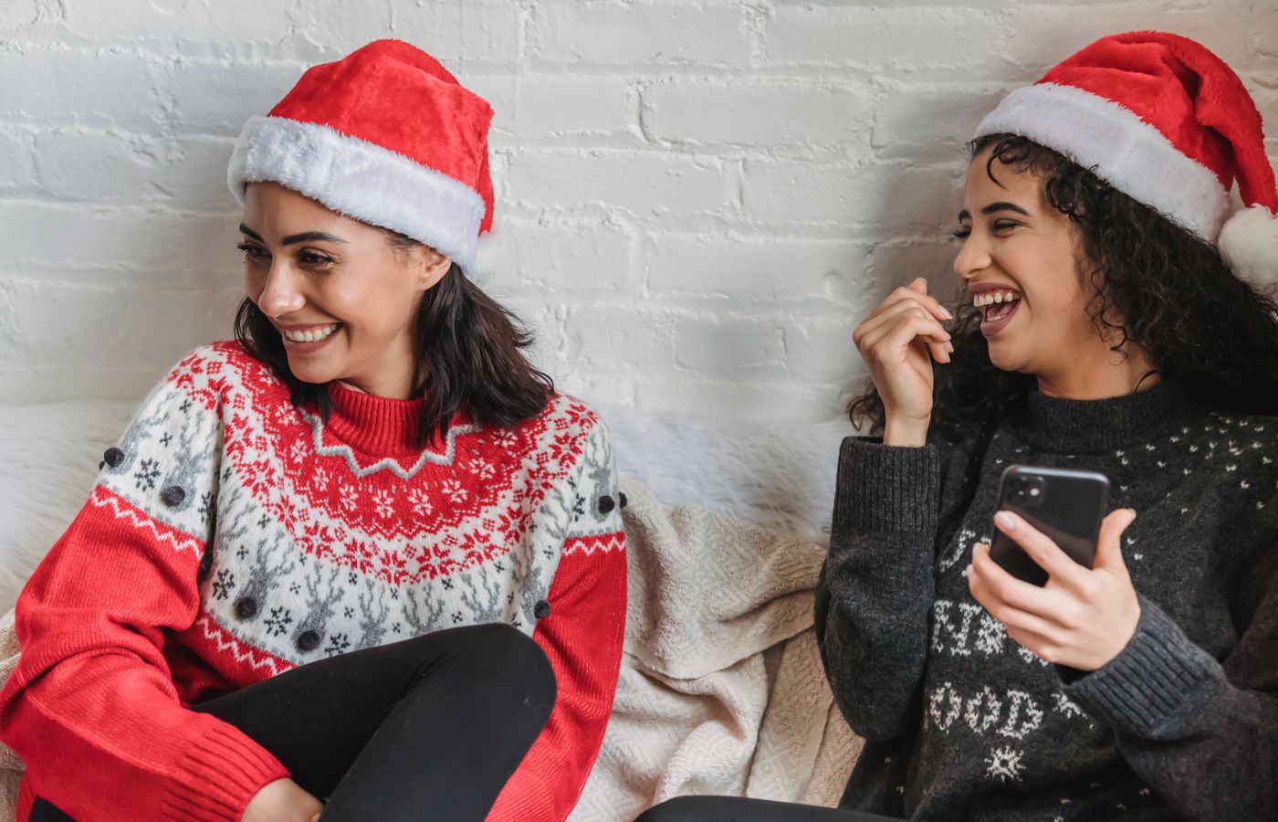 Two women in Santa hats sharing a joyful moment indoors during Christmas season.